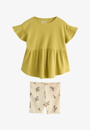 Soonimustriga sinepikollane lühikeste varrukatega ülaosa, millel on hõlmikpõhjaosa, sobitatud kreemja värvi lühikeste pükstega, millel on väikesed pruunid lillemustrid.