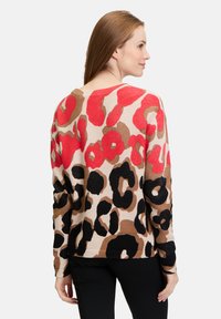 Knit sweater featuring a multicolored leopard print in red, black, and tan on a light background, with a relaxed fit and long sleeves.