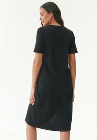 Schwarzes Baumwollmischkleid mit kurzen Ärmeln, knielang, runder Ausschnitt und lässiger Passform. Glatte Textur mit minimalen Details.