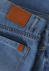 Denim jeans in light blue with a textured finish. Features brown leather patch with "TATUUM" label and accent stitching on pockets.