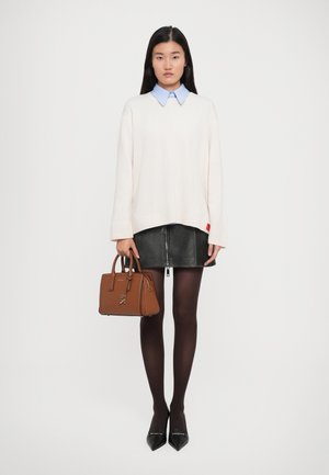 Woman wearing oversized white sweater over blue collared shirt, black leather mini skirt, sheer black tights, black pointed heels, holding brown handbag.