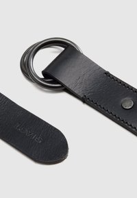 Μαύρη δερμάτινη ζώνη με κυκλική μεταλλική αγκράφα. Διαθέτει ραμμένες λεπτομέρειες και υφή στην επιφάνεια. Το λογότυπο είναι ορατό στο άκρο.