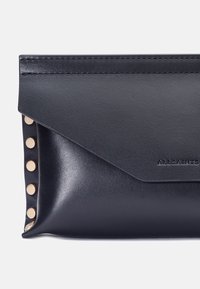 Svart läderkuvert med en kuvertdesign, prydd med guldtonade nitar på ena sidan och varum ärket diskret präglat.