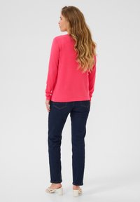 Roze trui met lange mouwen, gecombineerd met donkere spijkerbroek. De trui heeft een ronde halslijn en een rechte zoom.