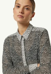 Black and white sheer blouse featuring a zigzag animal print, classic collar, button-down front, and long sleeves with cuffs.