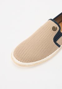 Botte slip-on en mesh beige avec une bordure bleu marine, bout rond et semelle en jute. Présente un petit logo accent près du col.