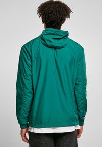 Grøn, letvægtsjakke med hætte, glat tekstur, elastiske manchetter og en afslappet pasform. Bagsiden har et enkelt design.