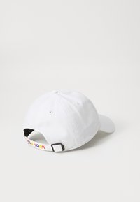Cappellino da baseball bianco con visiera curva. Presenta un testo "NEW YORK" multicolore sulla cinghia regolabile sul retro. Materiale in cotone.