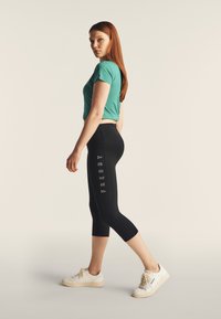 Leggings nere a vita alta con scritta 'FREDDY', abbinate a una maglietta aderente turchese e sneakers beige con dettagli testurizzati.