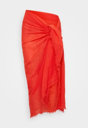 Κόκκινη πλεκτή φούστα σε περιτύλιξη φτιαγμένη από ελαφρύ ύφασμα. Διαθέτει μια στριμμένη ζώνη στη μέση και περιθώρια με φούντες. Απαλή υφή και ρέουσα σχεδίαση.