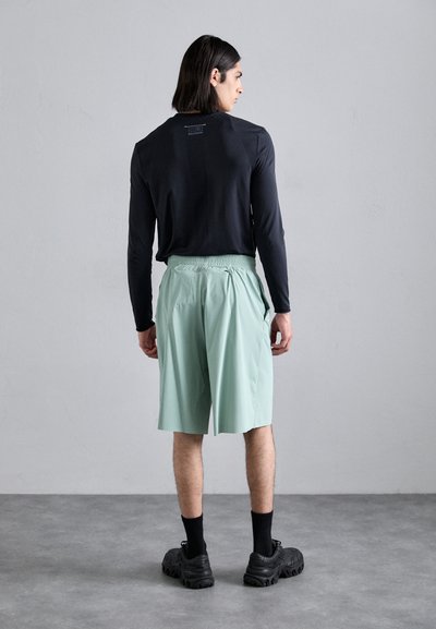 Haut noir à manches longues avec une texture côtelée, associé à un short vert menthe à taille élastique et des chaussures noires épaisses.