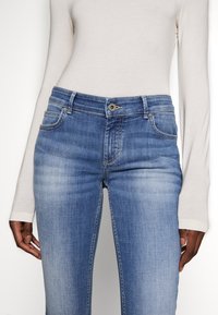 Skinny blue jeans made from denim, featuring a mid-rise waist, subtle fading, five pockets, and a classic button and zipper closure.