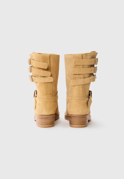 Botines de ante amarillos con un tacón de madera maciza, que presentan tres correas ajustables con hebillas de plata en la parte trasera para un detalle de diseño.