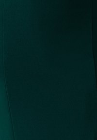 Dopasowana spódnica do kolan w głębokim zielonym kolorze, wykonana z gładkiej tkaniny; cechuje się subtelną fakturą i minimalną ilością szwów dla eleganckiego, opływowego wyglądu.