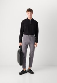 Black zip-collar long-sleeve shirt, gray fitted trousers, black loafers, and a black tote bag. Smooth fabric with tailored fit.