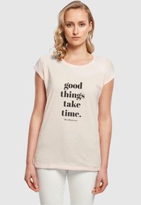 Lyserød t-shirt med korte ærmer lavet af bomuld, med sort tekst: "gode ting tager tid. #TrustTheJourney" fremtrædende vist.