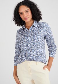 Camicia a maniche lunghe con un motivo geometrico blu, bianco e rosa. Presenta un colletto e una chiusura a bottoni, realizzata in un tessuto liscio.
