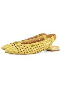 Zapatos amarillos trenzados con puntera afilada y parte trasera abierta, que cuentan con un tacón plano y forro de cuero marrón. Patrón texturizado en toda su superficie.