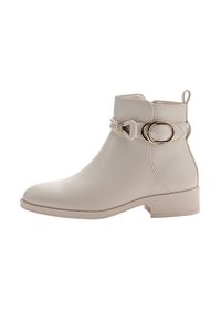 Botín beige con tacón bajo, cremallera lateral y tira decorativa de doble hebilla dorada en la parte superior de cuero liso.