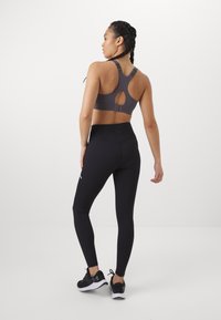 Gray sports bra with open back design, paired with black high-waisted leggings. Both are fitted and made of stretchy fabric. Black sneakers complete the look.