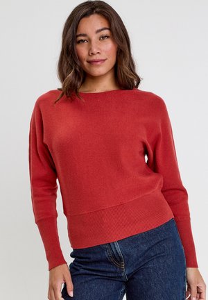 Roestrode, gebreide trui met een brede halslijn, geribde manchetten en zoom. Getailleerde pasvorm, zachte textuur. Model gecombineerd met hoog in de taille zittende donkere jeans.