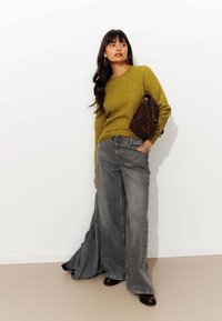 Pull en laine vert olive, jeans ample en denim gris, sac à bandoulière marron à imprimé léopard, associé à des chaussures sombres.