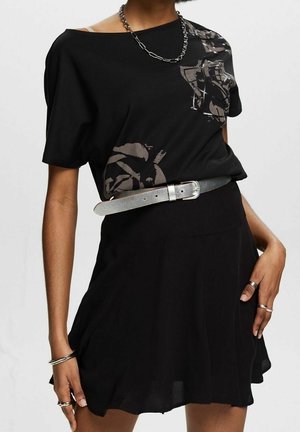 Zwart korte mouwtopje met een bloemenpatroon, gecombineerd met een zwarte skaterrok. Voorzien van een zilveren riem en sieradenaccenten. Zachte stoftextuur.