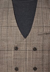 Brązowa i czarna kamizelka w kratę z głębokim dekoltem w serek. Posiada podwójnie zapięte guziki oraz teksturowany materiał zakrywający ciemną bluzkę.