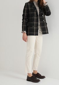 Černý kostkovaný dvouřadý sako, bílé tričko, krémové kalhoty po kotníky a tmavě hnědé texturované šněrovací boty.