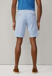 Shorts en coton bleu clair à coupe droite, poches arrière et détails de couture subtils, associés à des chaussures en daim marron.