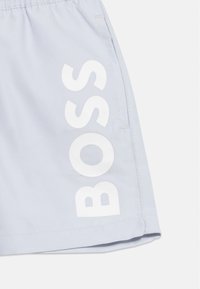 Φωτεινά μπλε σορτς με κάθετο λευκό λογότυπο "BOSS" στο αριστερό πόδι και εμφανείς ραφές στο πλαϊνό τσέπωμα.