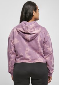 Zkrátená mikina s kapucňou v levandulovom tie-dye vzore. Má sťahovaciu kapucňu a dlhé rukávy. Vyrobená z mäkkého, priedušného materiálu.
