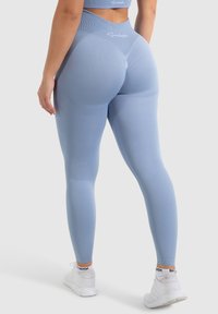 Leggings azzurri chiari realizzati in materiale elasticizzato, con vita alta e texture a costine, abbinati a scarpe da ginnastica bianche.