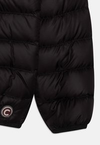 Svart pufferväst med kviltade sektioner, slät yta och logotypmärke. Tyget verkar lättviktigt med slim fit och elastisk nederkant.