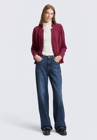 Burgundy blazer over a white turtleneck, paired with flared blue jeans. The outfit features a casual yet structured design.
