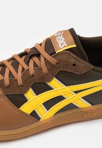 Baskets ASICS marron et jaune en cuir suédé et en cuir, au design basse, avec des lacets ronds et des détails perforés sur les côtés.