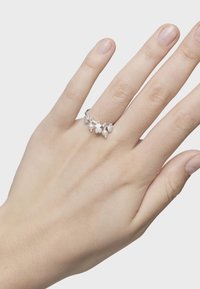 Anillo de plata con pequeños colgantes de estrella y corazón, adornado con perlas blancas, colocado sobre una mano con textura de piel suave.