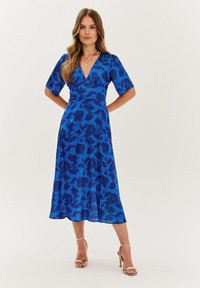Modré midi šaty s květinovým vzorem, krátkými nabíranými rukávy, výstřihem do V a vzdušnou siluetou, doplněné sandály na řemínky.