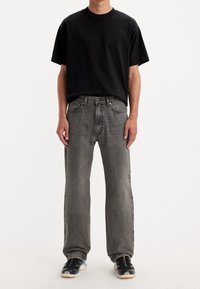 Svart bomullströja, avslappnad passform, kombinerad med grå denimjeans, rak bendesign, texturerad tyg, och svarta träningsskor med färgglada accenter.