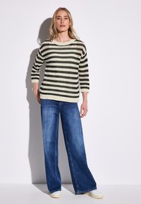 Gestreifter Strickpulli in Schwarz und Creme, mit lockerer Passform und drei Viertelärmeln, kombiniert mit weiten blauen Denim-Jeans.