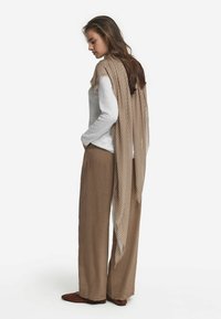 Écharpe rayée marron clair posée sur un haut à manches longues blanc, associée à un pantalon large beige et des chaussures à enfiler marron.