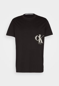 Černé bavlněné tričko s krátkými rukávy, na kterém je bílý nástřikový logo "ck" a text poblíž dolního levého rohu. Hladká textura, klasický střih u krku.