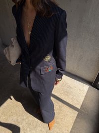 Jūrų laivyno smulkaus rašto blazeris su auksiniu akiu ir saulės siuvinėjimu, derinamas su atitinkamomis kelnėmis ir tan spalvos naginėmis kulniūkštėmis. Minkštos tekstūros rankinė, subtilūs papuošalai.