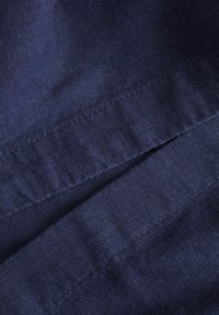 Navyblauwe stof met een subtiele textuur en lichte glans. Twee overlappende delen onthullen net gespen langs de randen.