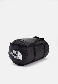 Black duffel bag made of durable fabric, featuring adjustable straps, buckles, and a prominent white logo. Oval shape with textured surface.