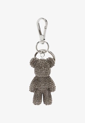 Breloczek z metalowym, srebrnym zapięciem, trzymającym małą figurkę misia pokrytą ciemnymi, błyszczącymi kryształkami.