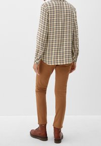 Camicia a quadri gialla e blu navy, pantaloni chino marroni e stivali in pelle marroni. Cuciture e dettagli dei bottoni visibili; vestibilità rilassata.