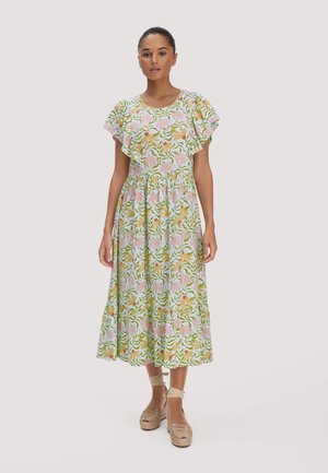 Vrouw staat in een midi-jurk met bloemenprint en geruite mouwen, en beige espadrilles met enkelbandjes, tegen een effen witte achtergrond.