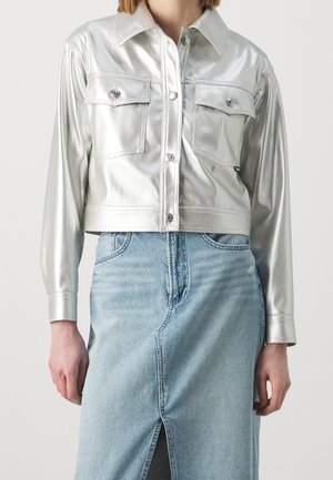 Zilverkleurige metallic cropped jas met lange mouwen, twee borstzakken en drukknoopjes. Gecombineerd met een lichtblauwe denim rok met een split.