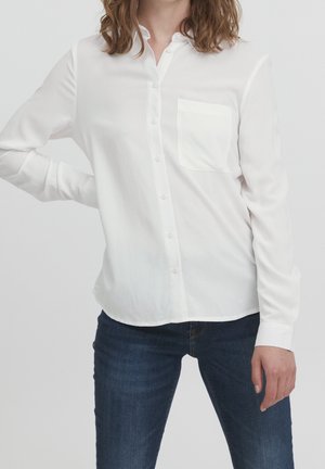 Chemise blanche à manches longues avec col, poche poitrine unique, texture lisse et coupe décontractée, associée à un jean en denim noir.
